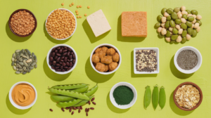 flat-lay image featuring 15 plant-based protein sources including lentils, chickpeas, tofu, tempeh, seitan, black beans, edamame, quinoa, seeds, peanut butter, green peas, spirulina, and nutritional yeast, arranged on a bright background